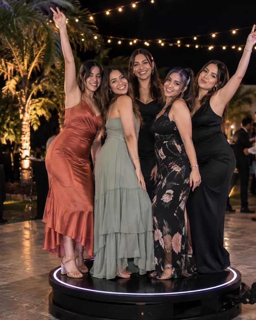 Five guests posing together on the 360° photo booth platform at an outdoor evening reception